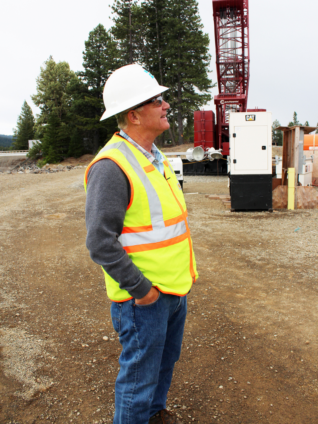 Tom observes construction while wearing a white hardhat and yellow safety vest